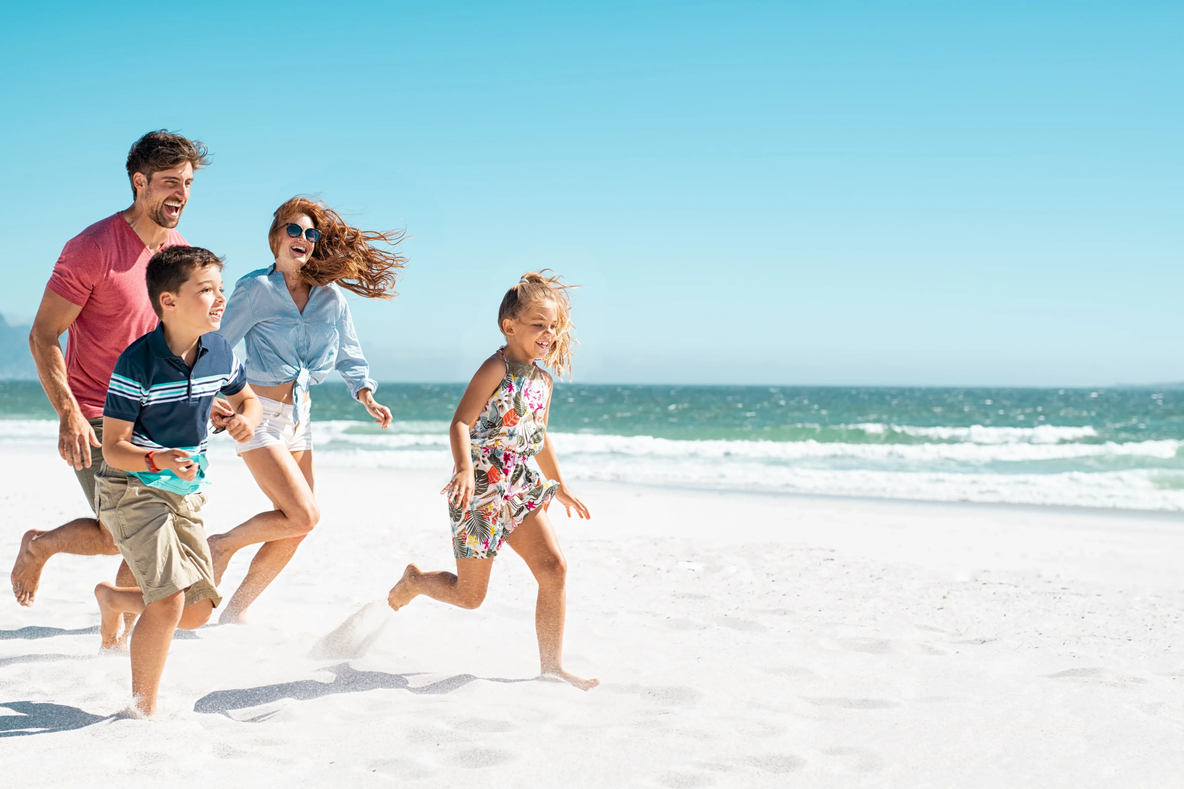 Family joyfully running on sandy beach.